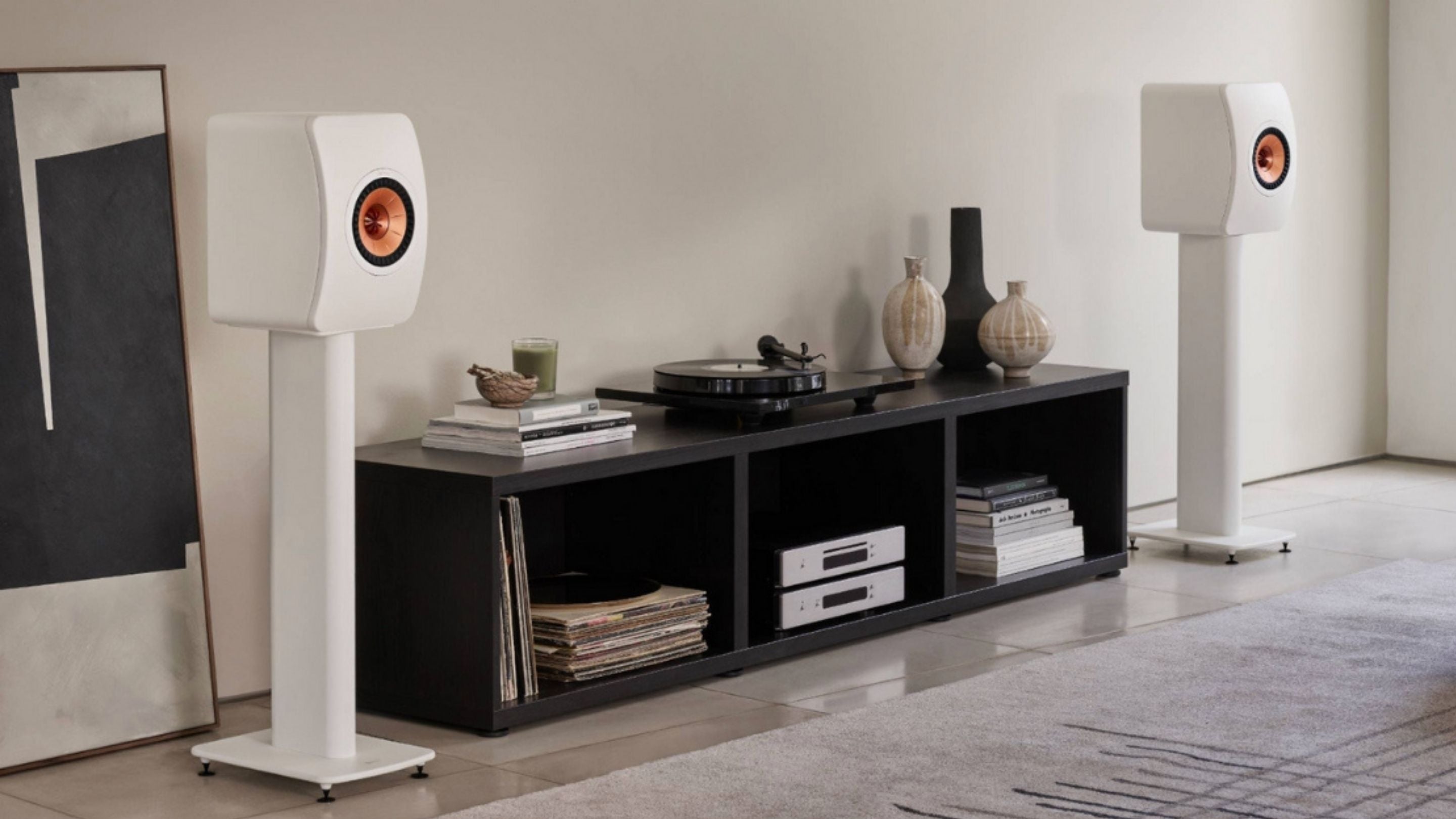 Modern living room with white KEF bookshelf speakers on stands, vinyl records and a turntable on a low media unit.