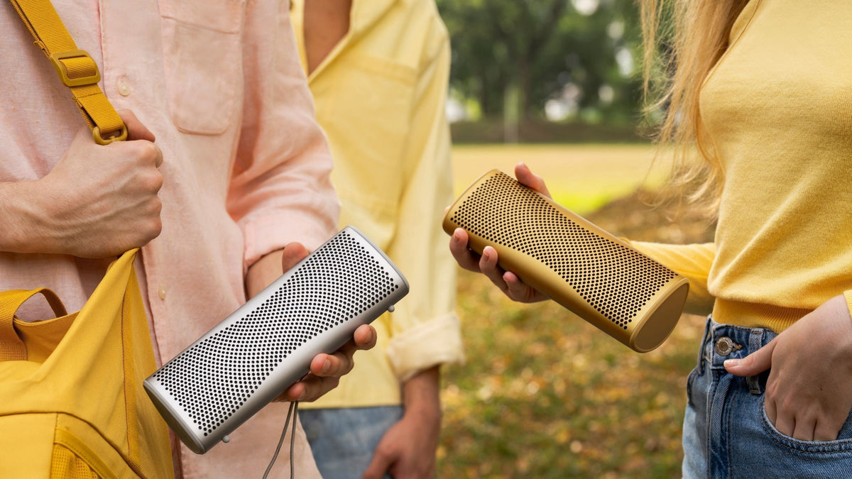 Two people holding a KEF Muo portable speaker in their hands 