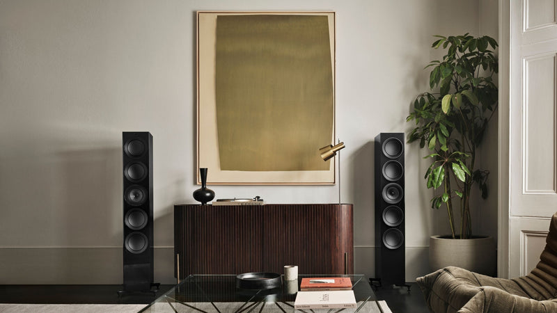 A pair of KEF Blade Two Meta white speakers displayed on a table within a stylish interior space.