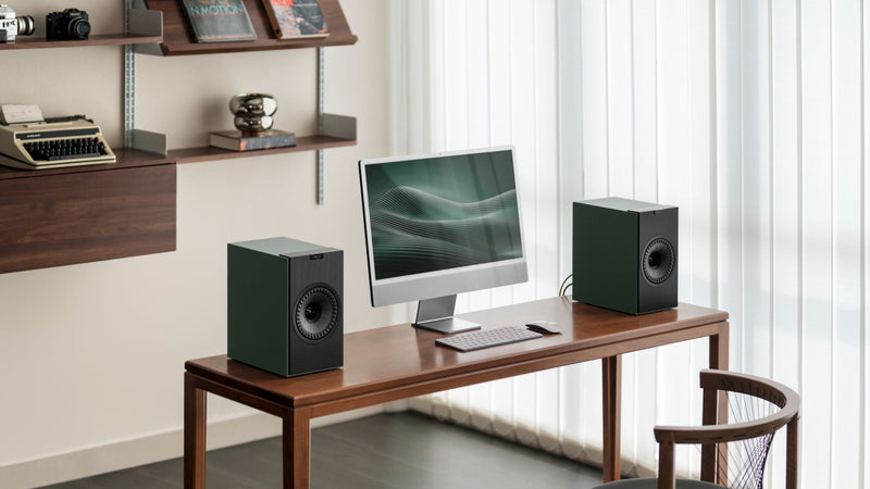  A workspace showcasing a computer, speakers, and a chair, highlighting the KEF Coda W speakers in a Moss Green finish.