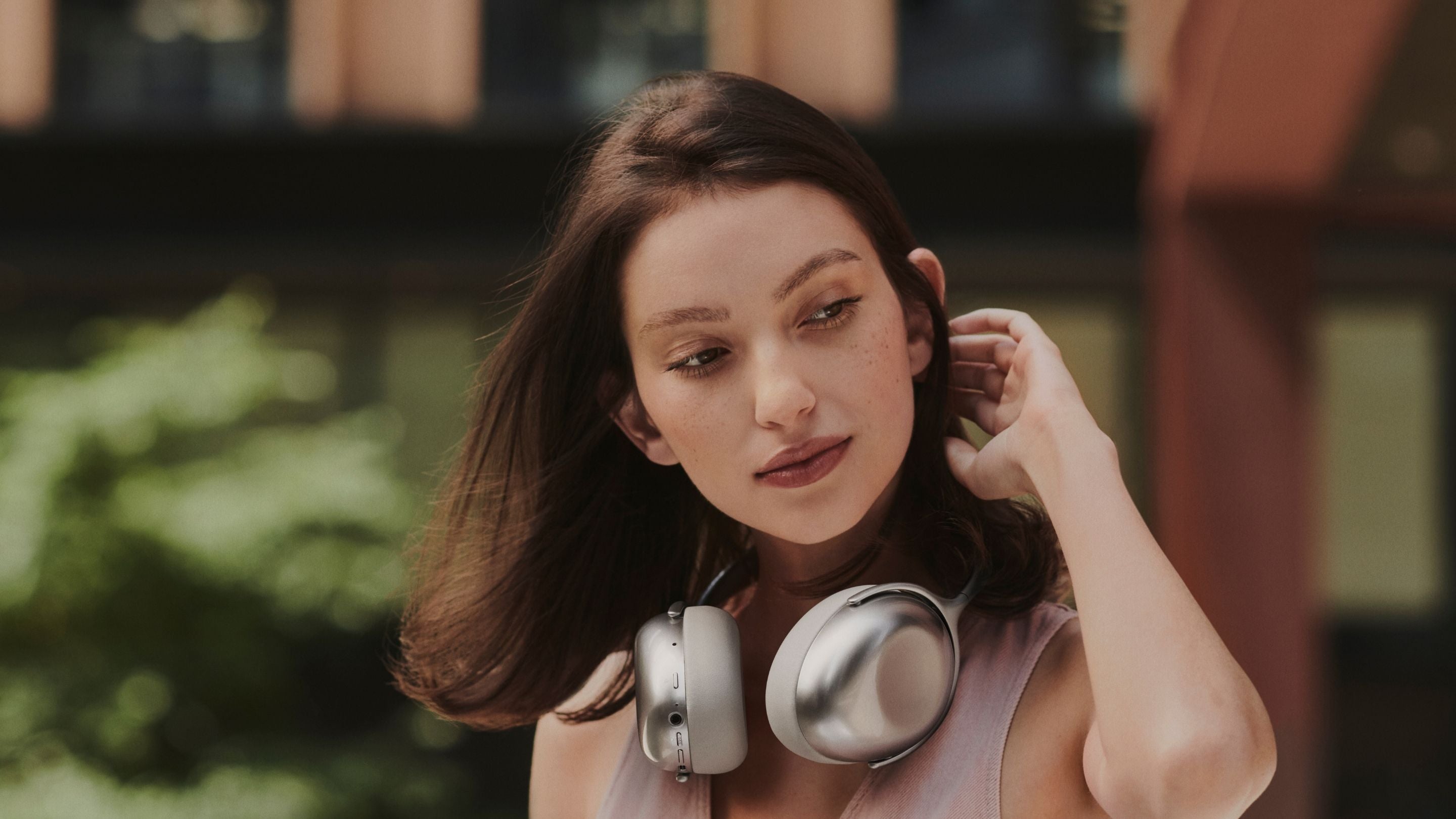 Lady wearing a KEF Mu7 headphone around her neck outside in a city space