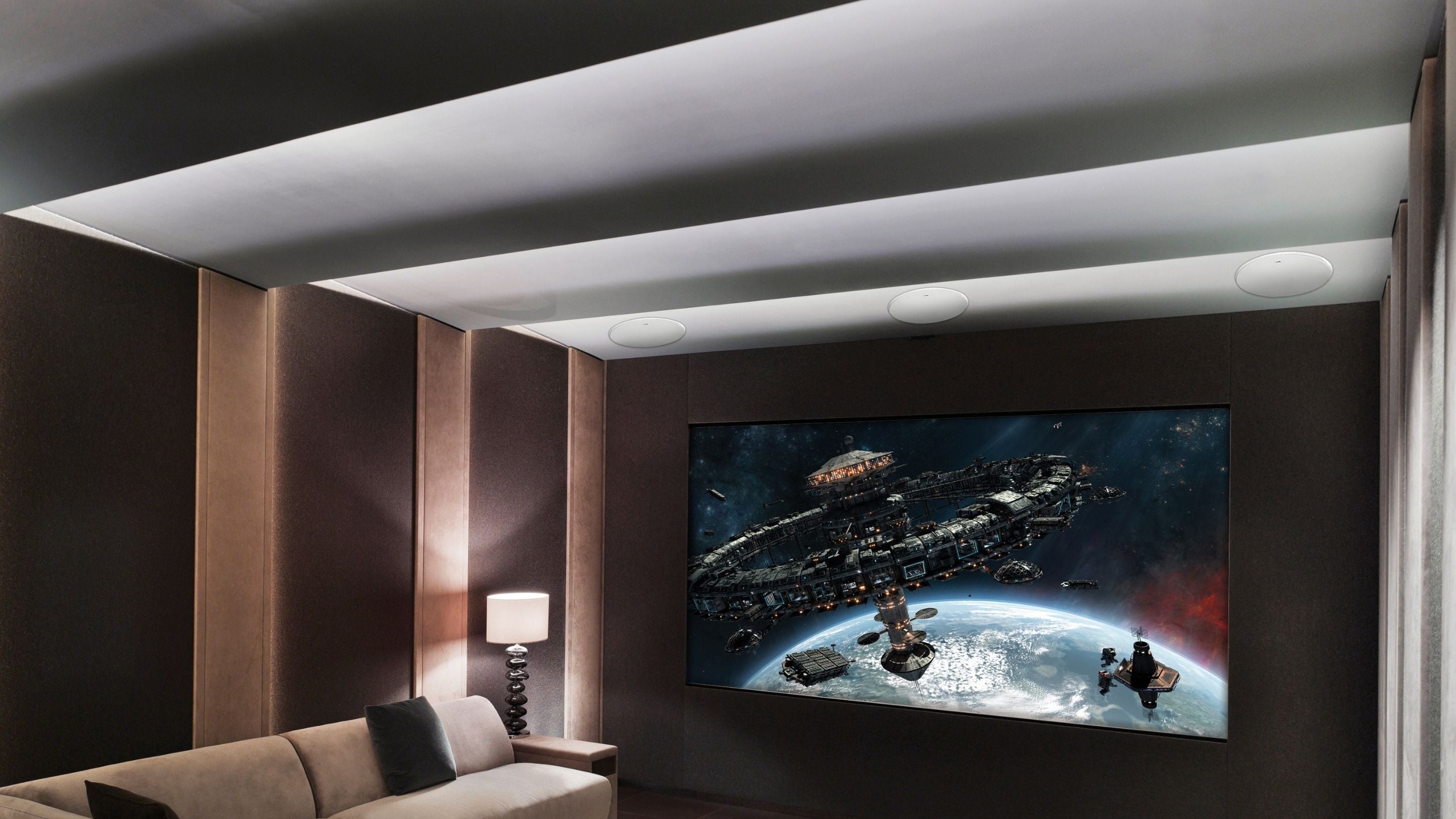 A home theater room featuring a large screen, couch, and KEF in-ceiling speakers for an immersive audio experience.