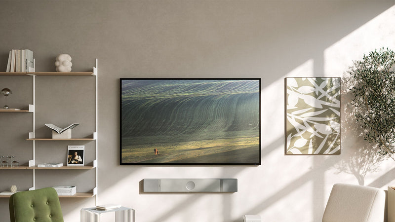 A living room scene showcasing a mounted  KEF XIO Soundbar to wall beneath the TV and a bookshelf in the background.